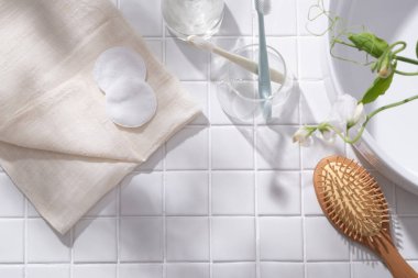 Pamuk yastıklı katlanmış bir havlu, cam içinde bulunan diş fırçaları ahşap bir fırça ve beyaz çiçek dalları. Ürününüzü göstermek için boş alan