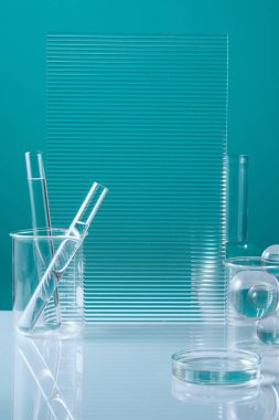Kaburgalı akrilik çarşaflar, içinde iki adet sıvı test tüpü bulunan bir deney şişesi ve diğer cam laboratuvar malzemeleri ayna masasında sergilenmektedir. Bilim kavramı