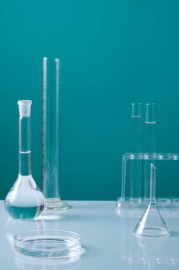 Test tüpleri ve bir sürü laboratuvar bardağıyla dekore edilmiş bir cam petri kabı. Asgari mavi arka plan. Ürün sunumu için ortada boş alan