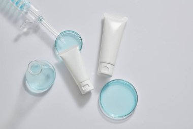 İçinde mavi sıvı bulunan farklı boyutlarda iki beyaz tüp, bir spiral boru tüpü ve bir erlenmeyer şişesi. Kozmetik ürün modeli