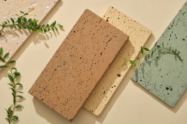 Bej arka planda farklı renklere sahip birkaç taş podyum düzenlenmiştir. Yeşil yapraklarla süslenmiş. Ürünü tanıtmak için boş alan