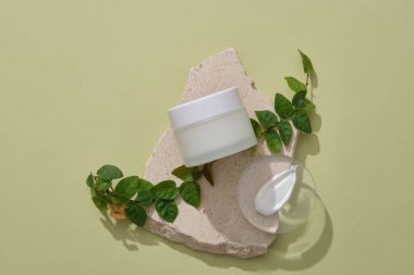 Boş etiket kavanozu, yeşil yaprakları ve yuvarlak şekilli krem desenli şeffaf bir podyumu olan kırık bir taş podyum. Cilt bakımı kavramı