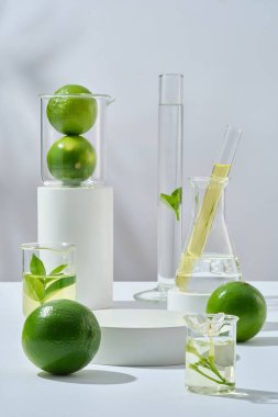 Laboratuvar camları ve limonla dekore edilmiş boş, beyaz bir podyum. Lime (Citrus aurantiifolia) sağlık ve cilt için birçok avantajlara sahiptir.