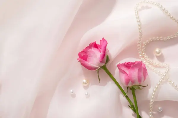 在白色雪纺面料的背景下 玫瑰装饰着珍珠和珍珠项链 玫瑰精油有许多有益的特性 — 图库照片