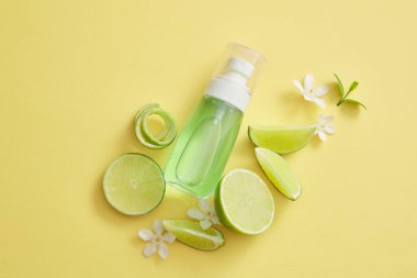 Çiçekler ve limon dilimleri ile süslenmiş, Lime 'den (Citrus aurantiifolia) elde edilen yeşil sıvıyla dolu şeffaf bir pompa şişesinin düz yatağı. Doğal kozmetik ürünleri. Markasız maket