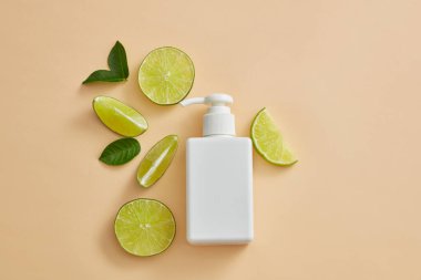 Açık arkaplana yeşil yapraklar ve limon dilimleriyle yerleştirilmiş boş etiket pompa kutusu. Lime (Citrus aurantiifolia) özetinin kozmetik ürün sunumu için boş etiket