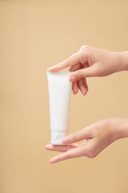 Beyaz, boş bir etiket tüpü, güzel bir kadın eli tarafından bej arka planda tutulur. Marka modeli. Doğal organik kaplıca ürünleri