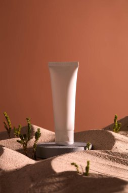 Taş kürsüde duran boş bir etiket beyaz tüp. Etrafı kum ve küçük yeşil ağaçlarla kaplı. Kozmetik ürün modeli
