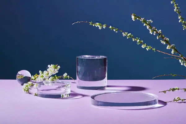 暗い背景の上に 多くの幾何学的な形をしたガラス透明な表彰台が白い花の枝で表示されます 製品を表示する表彰台の空白スペース — ストック写真