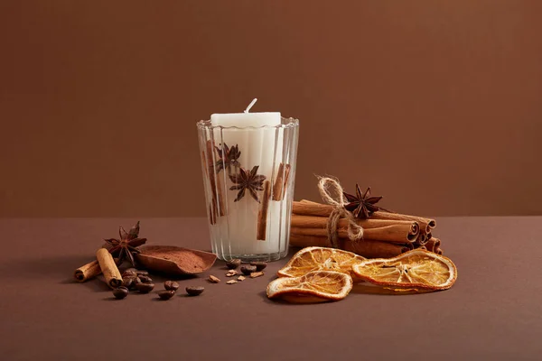 Biała Świeca Umieszczona Przezroczystej Szklance Kilka Paluszków Cynamonowych Ziarna Kawy — Zdjęcie stockowe