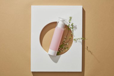 Beyaz podyum ve çiçek dallarıyla süslenmiş güzellik kozmetik promosyonu için boş etiketli pembe şişe.