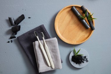 Siyah bambu, havlu ve gri arka planda diş fırçası içeren diş bakımı konsepti. Ahşap tepside ürün reklamı için boş yer var.