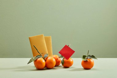 Minimalist pastel arka planda süslenmiş bazı mandalinalar ve sarı zarflar. Ön manzara. Tet tatil konsepti