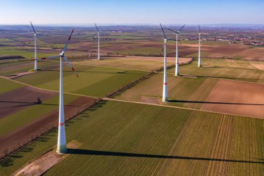 Aerial view of tall wind turbines between fields in the winter sun