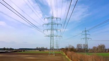 Almanya 'nın güneşli havasında kırsal alanlara kurulmuş kabloların ve yüksek voltajlı elektrik direklerinin hava görüntüsü.