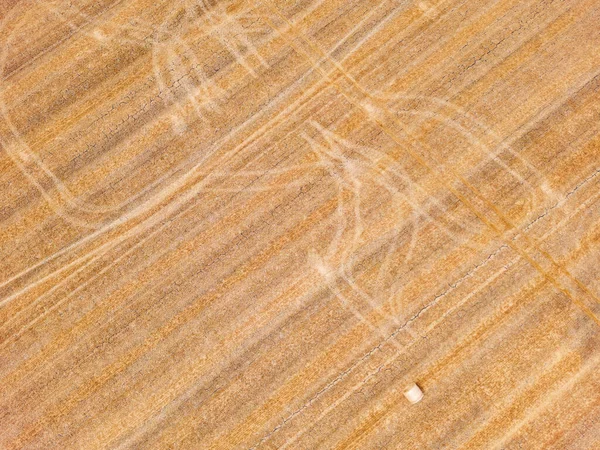 Striking tracks and patterns from a tractor on a dry agricultural field with straw bales, aerial view from Germany