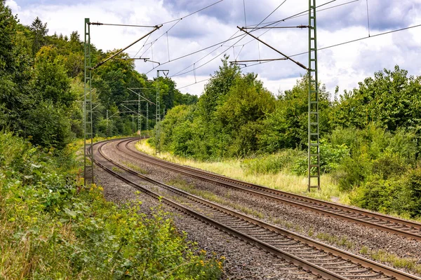 Two tracks of an electrified railroad line through green nature next to a noise barrier through rural Bavaria, Germany