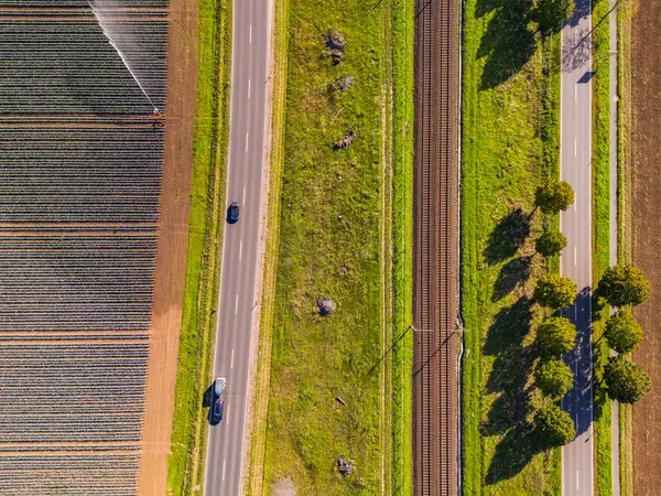 農業分野に隣接する2本の道と田の隣に2本の線路を持つ鉄道線 — ストック写真