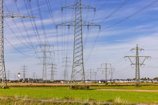 stock image Countless power poles and power lines in nature in front of houses of a city in background