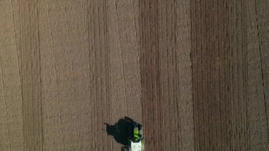 Kahverengi bir tarlada toprağı süren traktörün hava görüntüsü görüş alanından geçiyor.