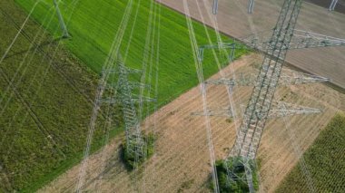 Kırsal bölgede, iki yüksek voltajlı sütun ve güç hatları arasında uçan bir hava aracı.