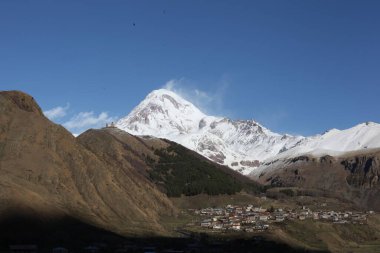 Güneşli günde Terek Vadisi ve köyü, Kazbek dağı ve Gergeti Trinity Kilisesi Stepantsminda Gürcistan Nisan 2017. Yüksek kalite fotoğraf