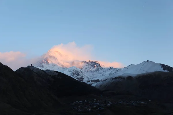 Terek Vadisi ve köy, Kazbek dağı pembe bulutlar içinde ve Gergeti Trinity Kilisesi gündoğumunda Stepantsminda Georgia Nisan 2017. Yüksek kalite fotoğraf