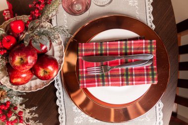 Elegant holiday table setting featuring a red plaid napkin, apples, and festive decorations. Ideal for Christmas dinner ambiance and seasonal celebrations, creating a warm and inviting atmosphere.