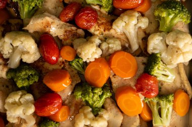 Brokoli, karnabahar, havuç ve kiraz domatesleri de dahil olmak üzere canlı sebzeli kızarmış tavuk göğsü, sağlıklı ve sağlıklı bir yemek sunumu oluşturur..