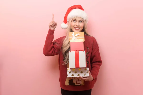 Portrait of happy Caucasian young woman in santa claus hat with gift box over pink background