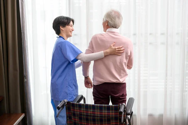 stock image An Asian nurse taking care of an elderly man getting up from wheelchair at senior healthcare center.