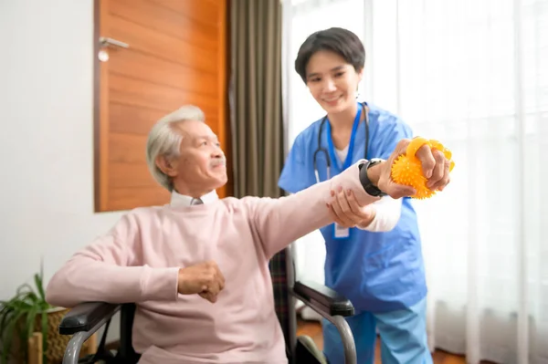 Asian nurse taking care of an elderly man sitting on wheelchair , doing hand exercises at  senior healthcare center.