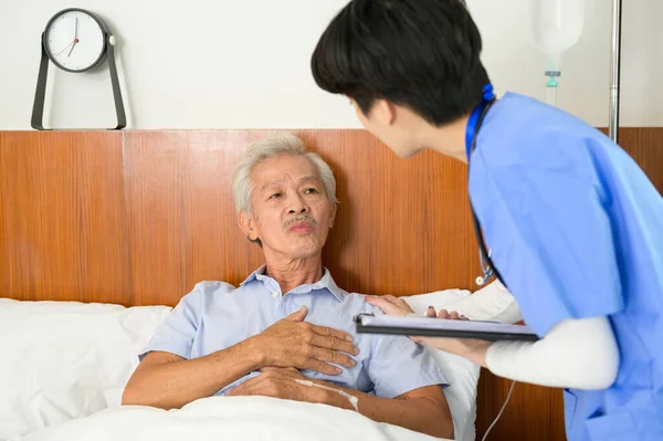 An Asian nurse taking care of an elderly man lying on patient bed at  senior healthcare center.