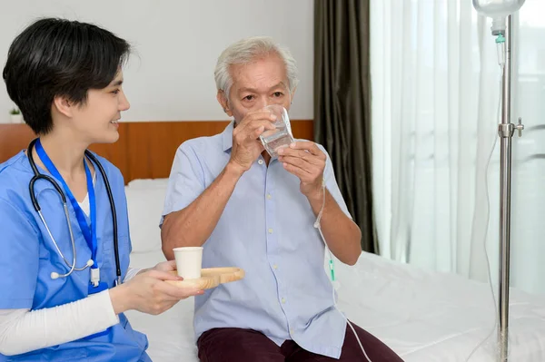 An Asian nurse giving an elderly medicine at  senior healthcare center.