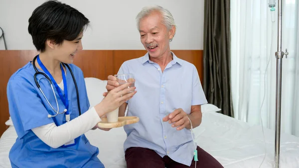 An Asian nurse giving an elderly medicine at  senior healthcare center.