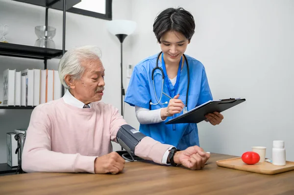An Asian nurse checking elderly man blood pressure and heart rate with digital pressure gauge at senior healthcare center.