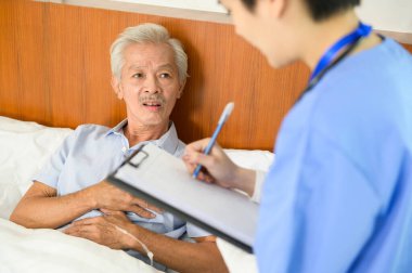 Yaşlı bir adamla ilgilenen Asyalı bir hemşire yaşlılar sağlık merkezinde hasta yatağında yatıyor..