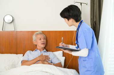 Yaşlı bir adamla ilgilenen Asyalı bir hemşire yaşlılar sağlık merkezinde hasta yatağında yatıyor..