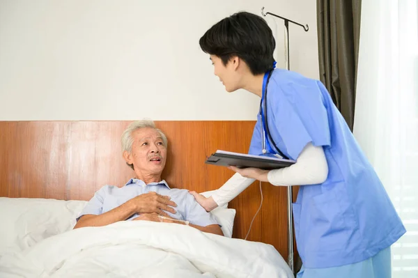 An Asian nurse taking care of an elderly man lying on patient bed at  senior healthcare center.