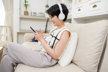 Evde müzik dinleyen kulaklık takan Asyalı bir genç. 