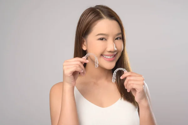 一名年轻的微笑女性 在白色背景工作室 牙齿保健和牙齿矫正的概念下 手持无创矫形器架 — 图库照片