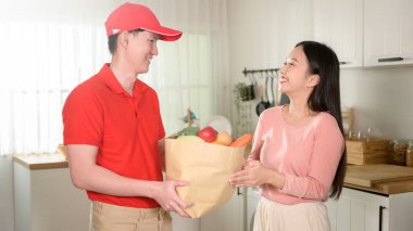 Asyalı genç adam kırmızı üniformalı, elinde sağlıklı meyve sebzeleri olan mutfak arka planındaki müşteriye gönderildi. 