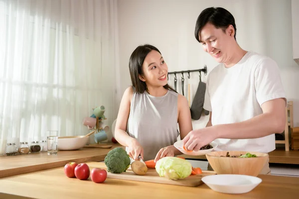 An Asian young couple enjoy cooking with healthy vegetables and fruits ingredients in kitchen at home , healthy wellness lifestyle concept.