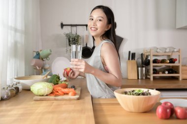 Evde taze su içen Asyalı genç bir kadın. Sağlıklı yaşam tarzı kavramı. 