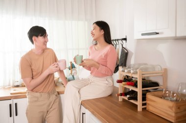 Mutlu genç Asyalı çift sabahları mutfakta kahve içip rahatlıyor.