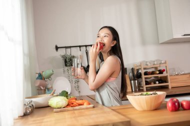 Evde, mutfakta elma tutan Asyalı genç bir kadın. Sağlıklı yaşam tarzı kavramı. 