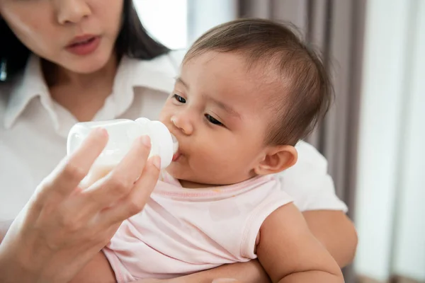A baby girl is drinking milk bottle in mother arms, family, child, childhood and parenthood concept