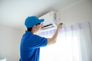 Asyalı genç bir teknisyen mavi üniformalı evde klima temizliyor.