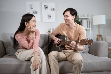 Mutlu genç Asyalı çift evdeki oturma odasında gitar çalarak şarkı söylüyor.