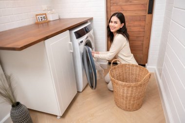 Mutlu Asyalı genç kadın evde çamaşır yıkıyor, sağlıklı yaşam tarzı konsepti.